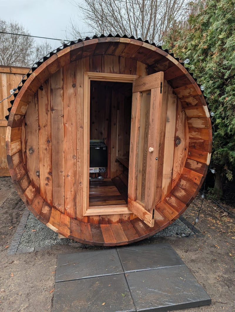 Load image into Gallery viewer, Wooden barrel-sauna with an open door, set outdoors.