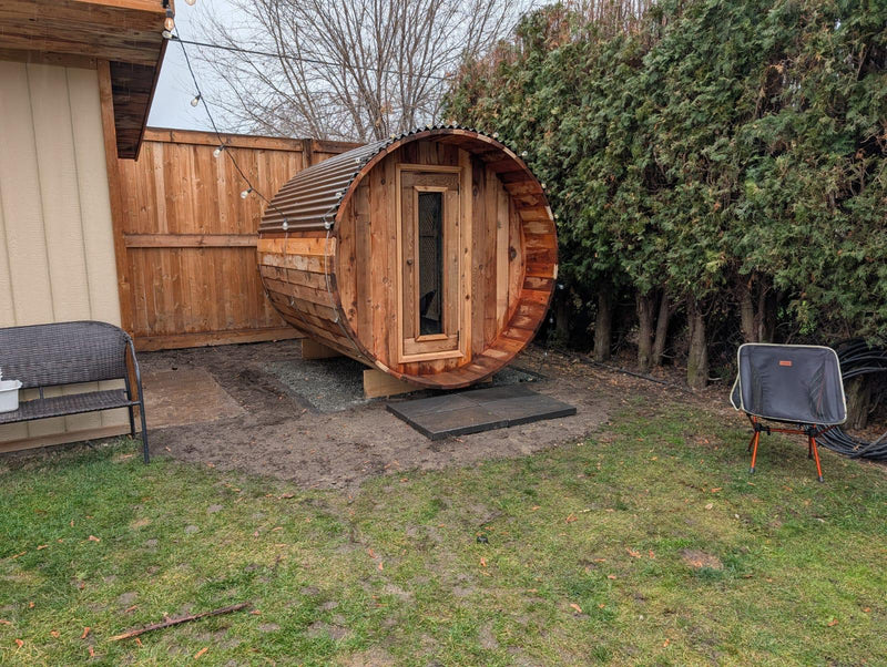Load image into Gallery viewer, Wooden barrel-shaped sauna in a backyard setting with grass and trees.
