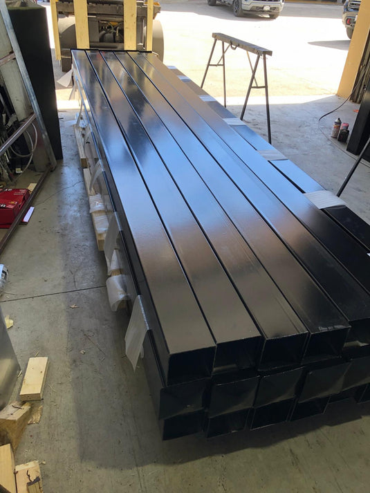Black powder-coated metal fence posts ready for shipping.
