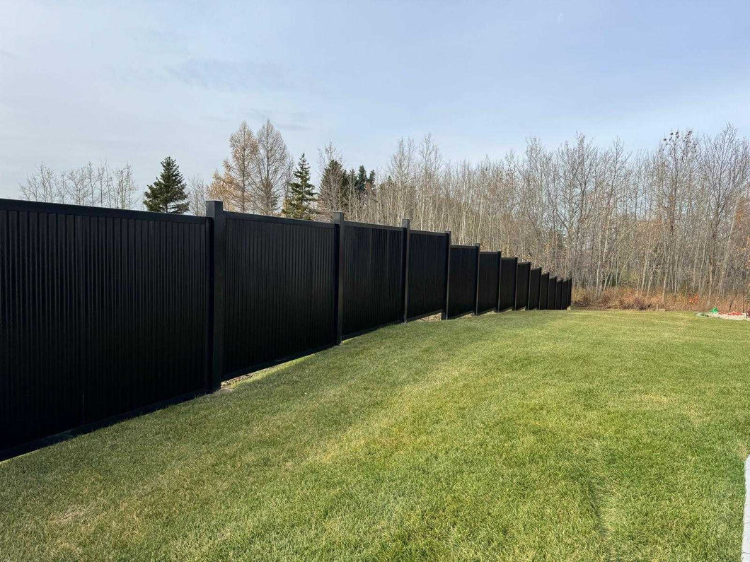 Black corrugated metal fence panels in a residential setting with wooded background.