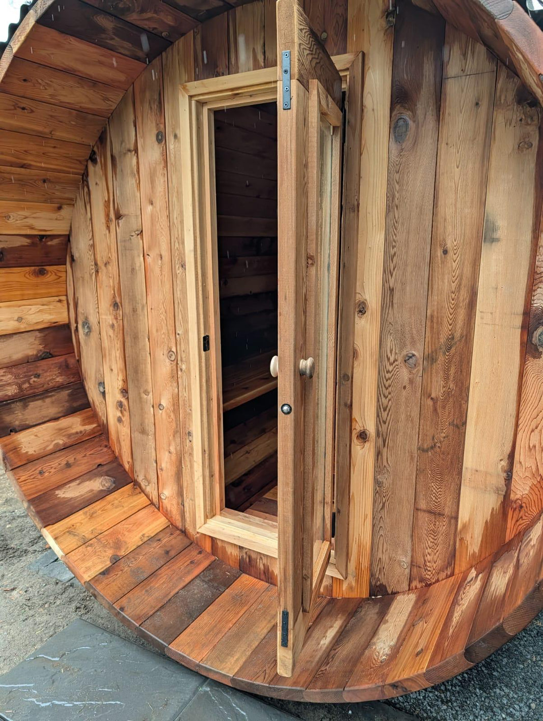 Wooden barrel sauna with an open door revealing a interior.